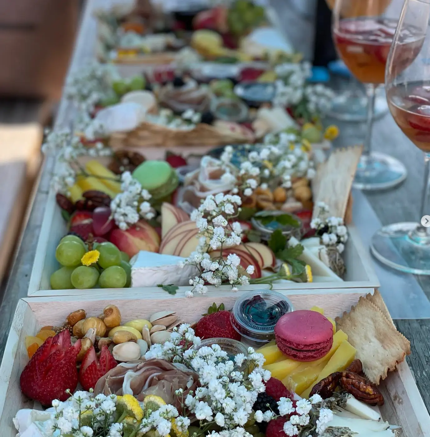 A long row of grazing boards with flowers and glasses of rosé on the Let It Brie patio table