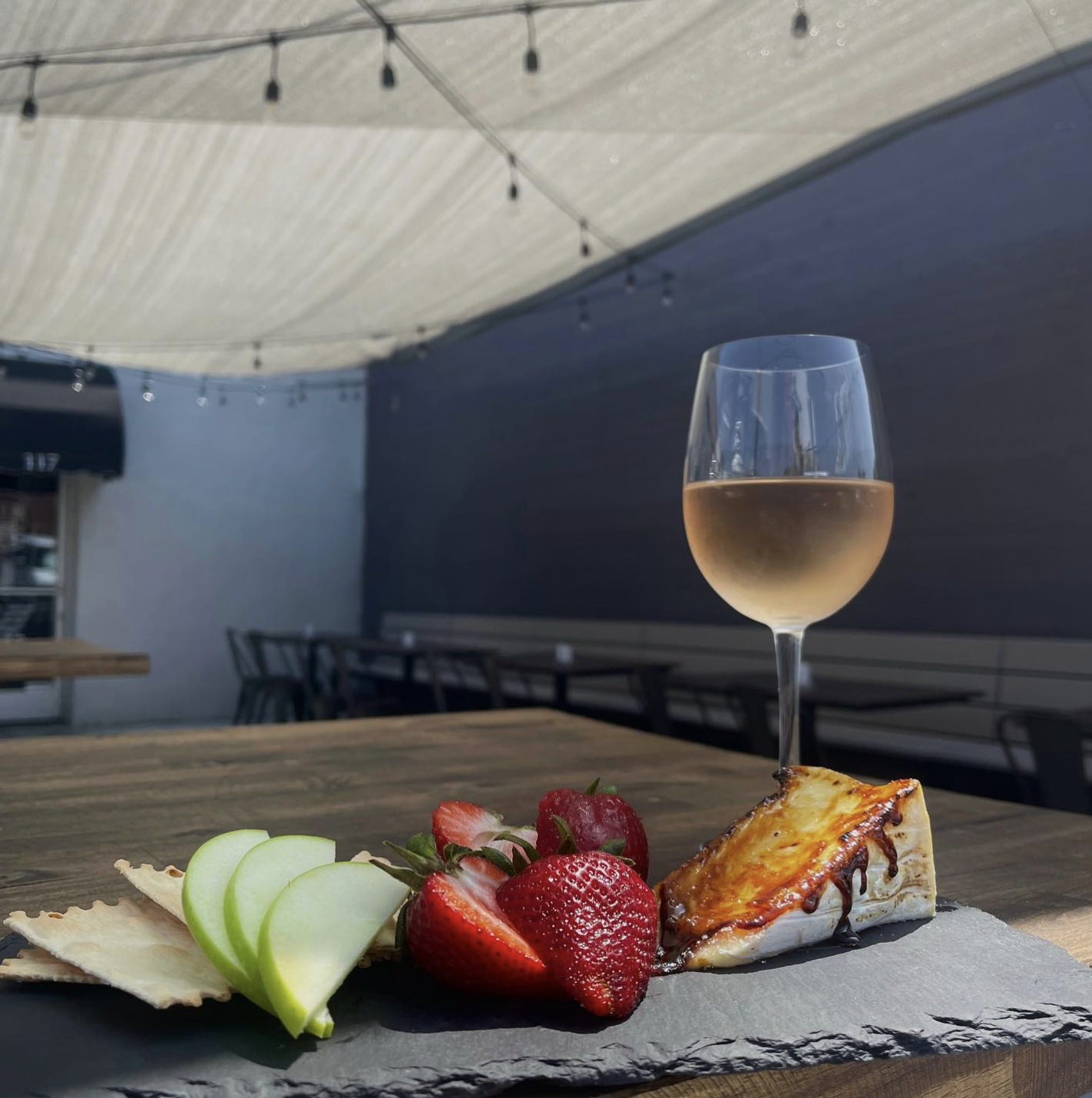 Glass of rosé and a baked brie board on the Let It Brie patio under string lights